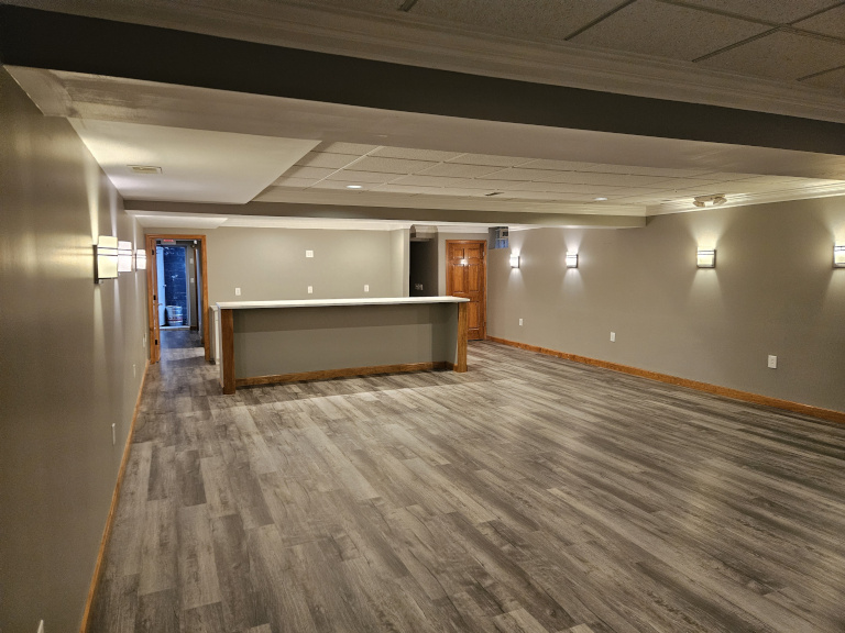 Lower level lounge — bar counter, sconce lighting, LVP flooring